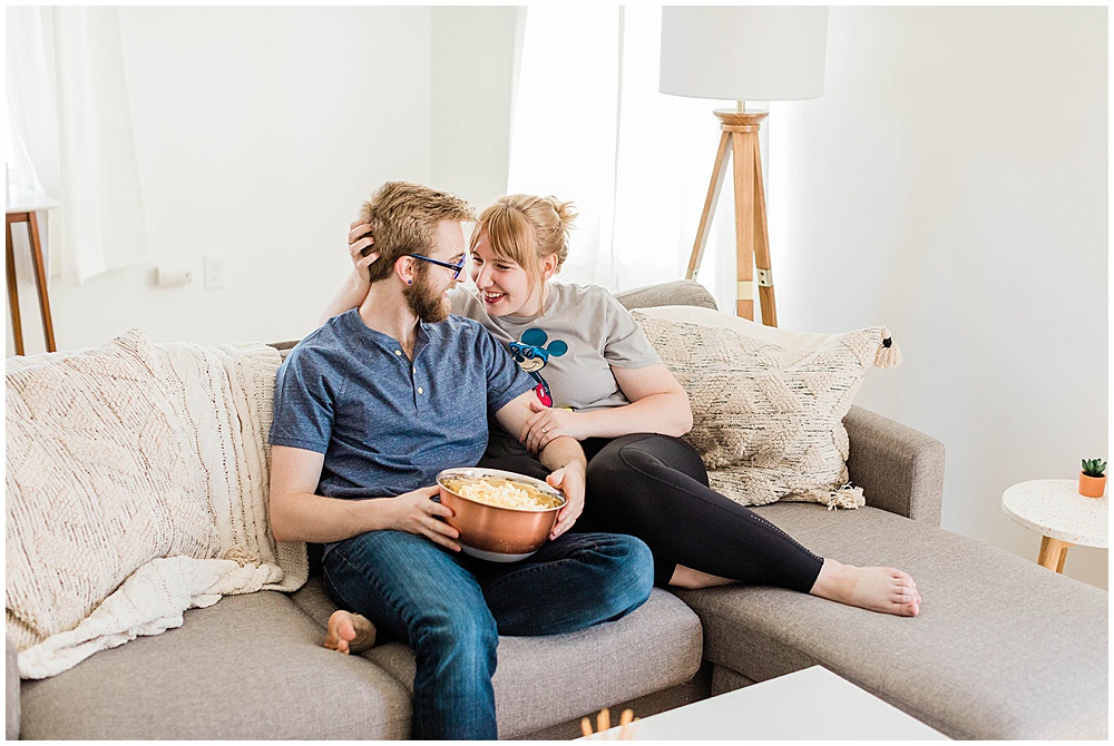 Affectionate couple cuddling on couch for weekly date night with a bowl of popcorn