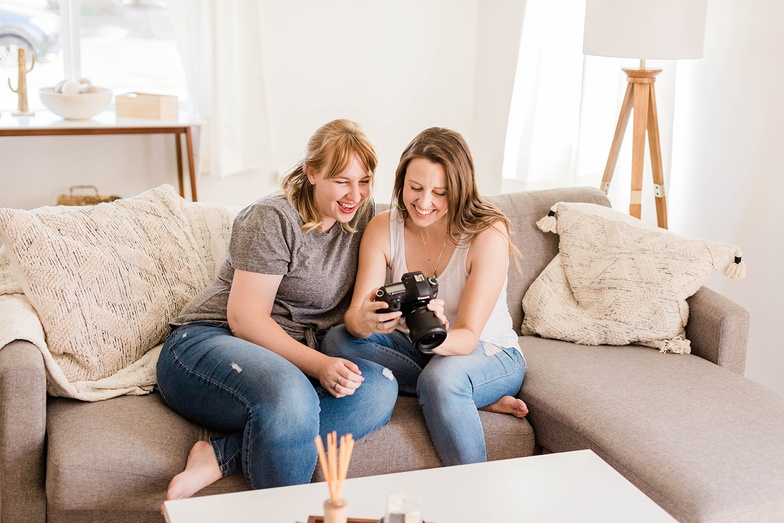 two women sitting on couch looking at the back of a digital camera