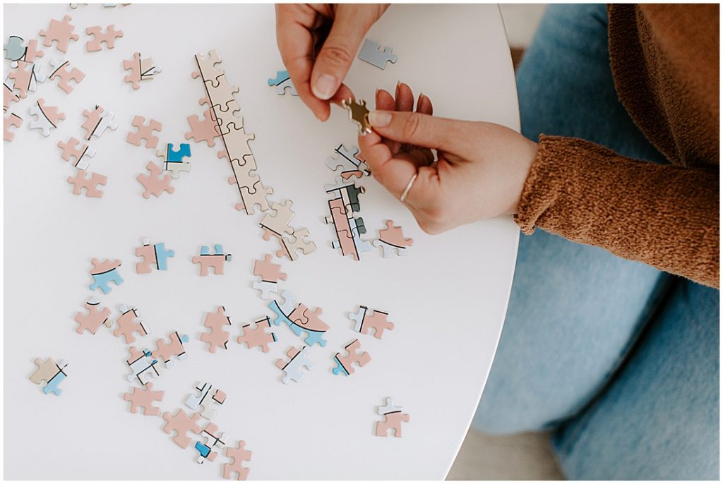 14 At Home Date Ideas - game night woman putting together a puzzle that is pink blue and white none of the image is discernible yet
