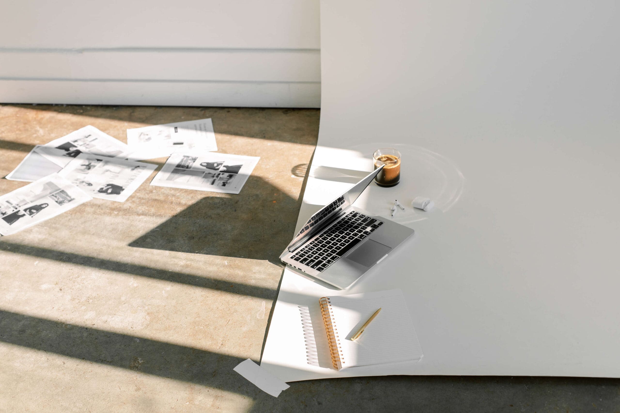 computer on the floor of a photography studio next to a coffee and some art prints