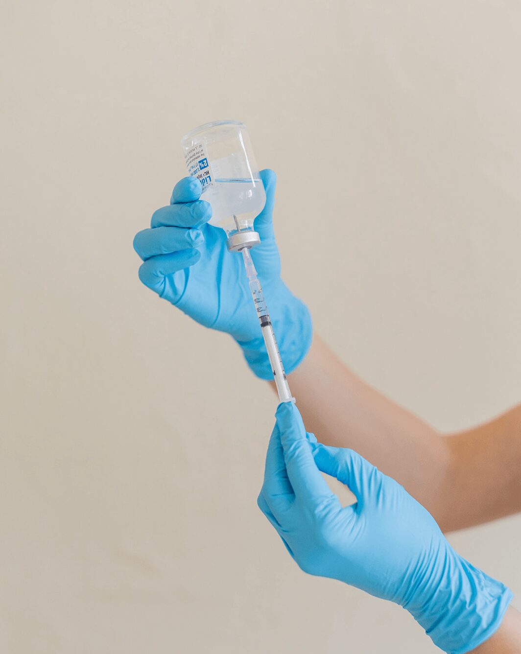 white woman wearing blue glues with a syringe in an overturned bottle of clear liquid for medical spa procedures